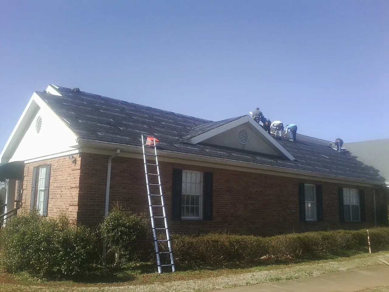 Crew tearing shingles off a brick ranch roof with a ladder set — Metal Roof Repair work by our crew in Cedartown