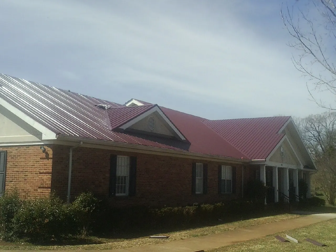 Red metal roof with gabled entries on a long brick building, from a Hail Damage Roof Repair job in Cedartown
