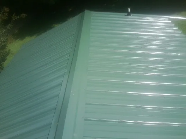 New green metal panels meeting at the ridge of a roof — Flat Roof Repair work by our crew in Cedartown