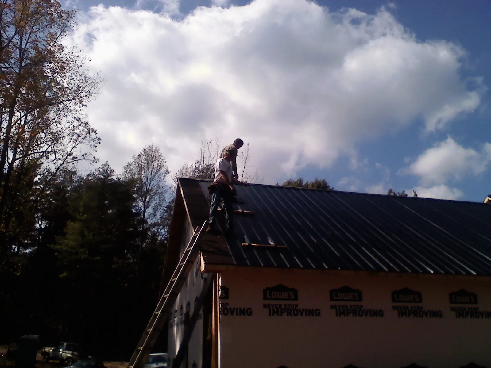 Roofer fastening dark metal panels high against a cloudy sky, from a Roof Inspection job in Cedartown