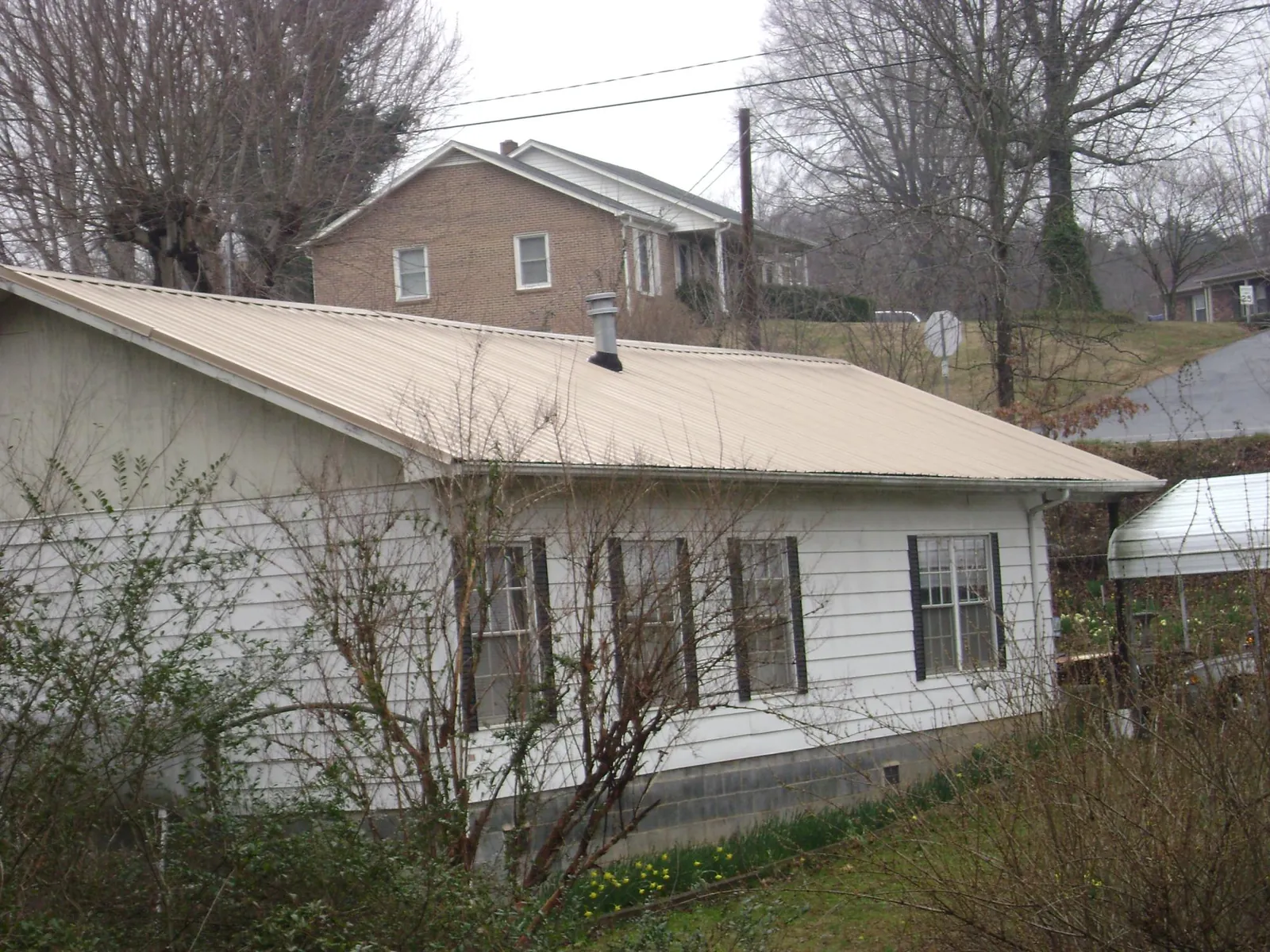 Tan metal roof on a white sided house set into a hillside — Commercial Roofing by Roofing Brothers in Cedartown